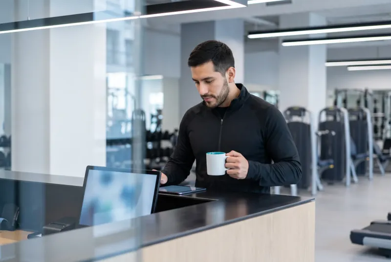 Dueño de un gimnasio con una taza revisa su tablet en la recepción.